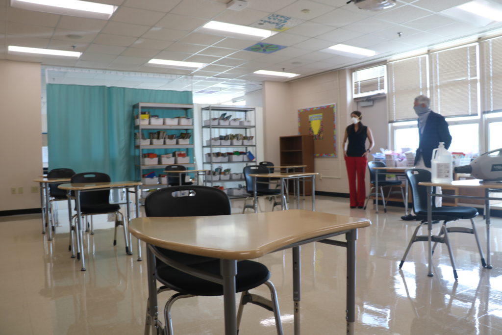 Two school employees stand in a socially distanced classroom.