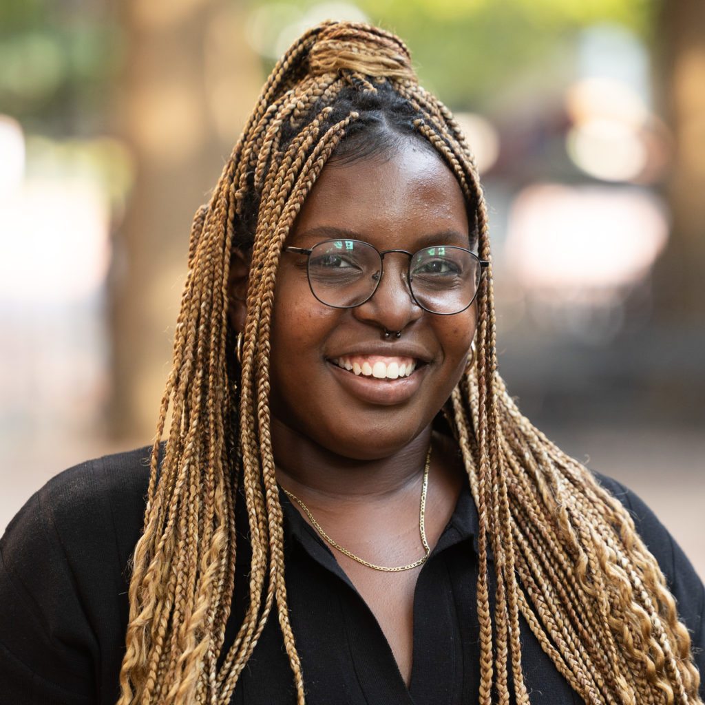 Woman with long braids and glasses smiling at camera for headshot