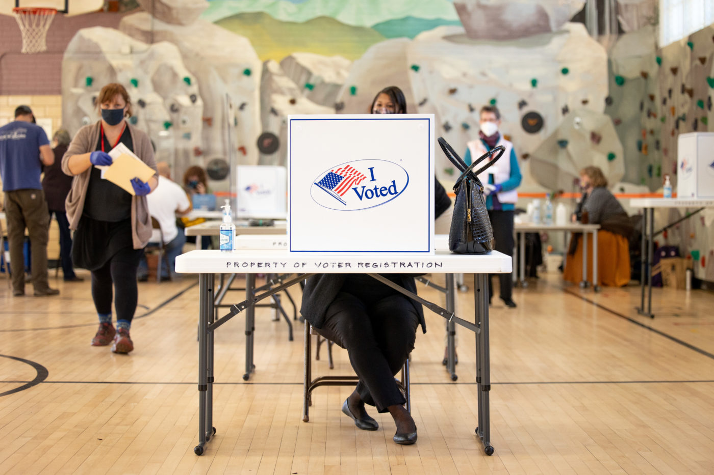 A person sits at a voting booth surrounded by other people in a gymnasium.
